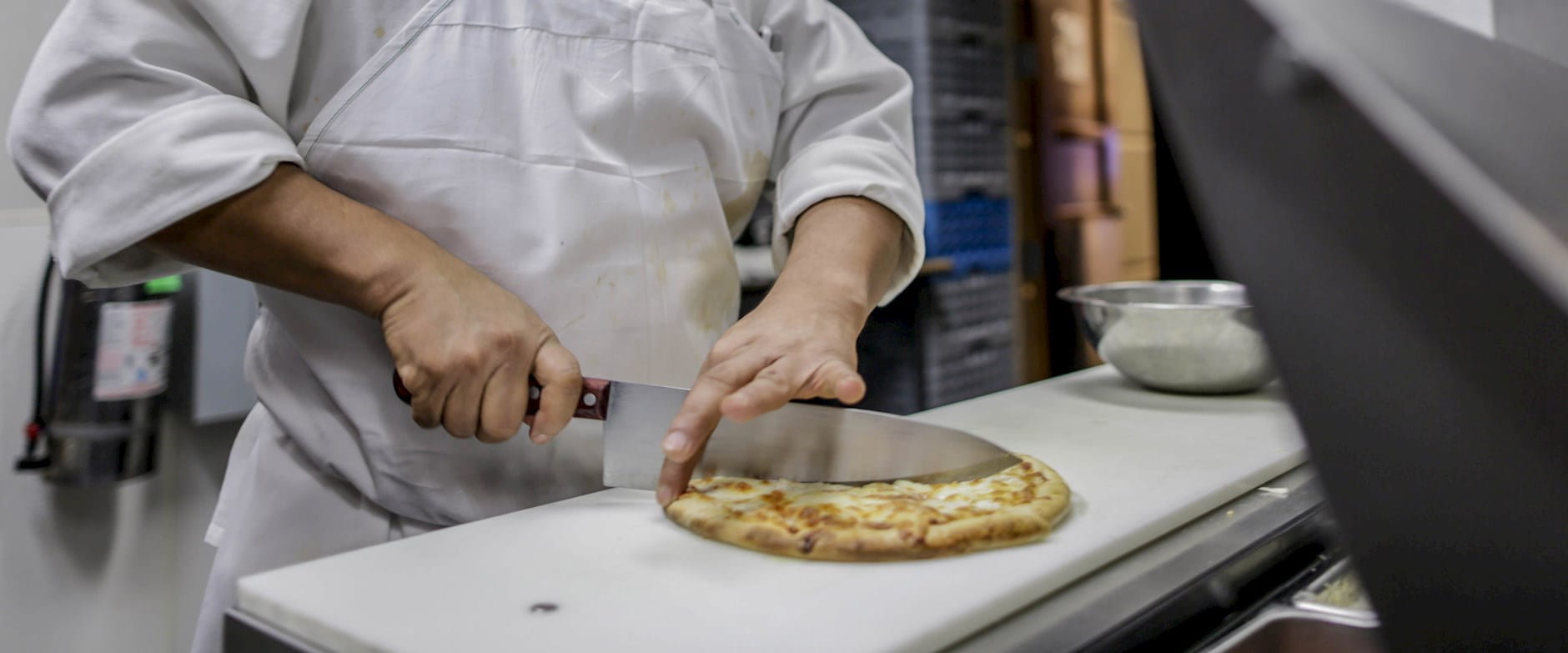A chef slices a cheese pizza in kitchen