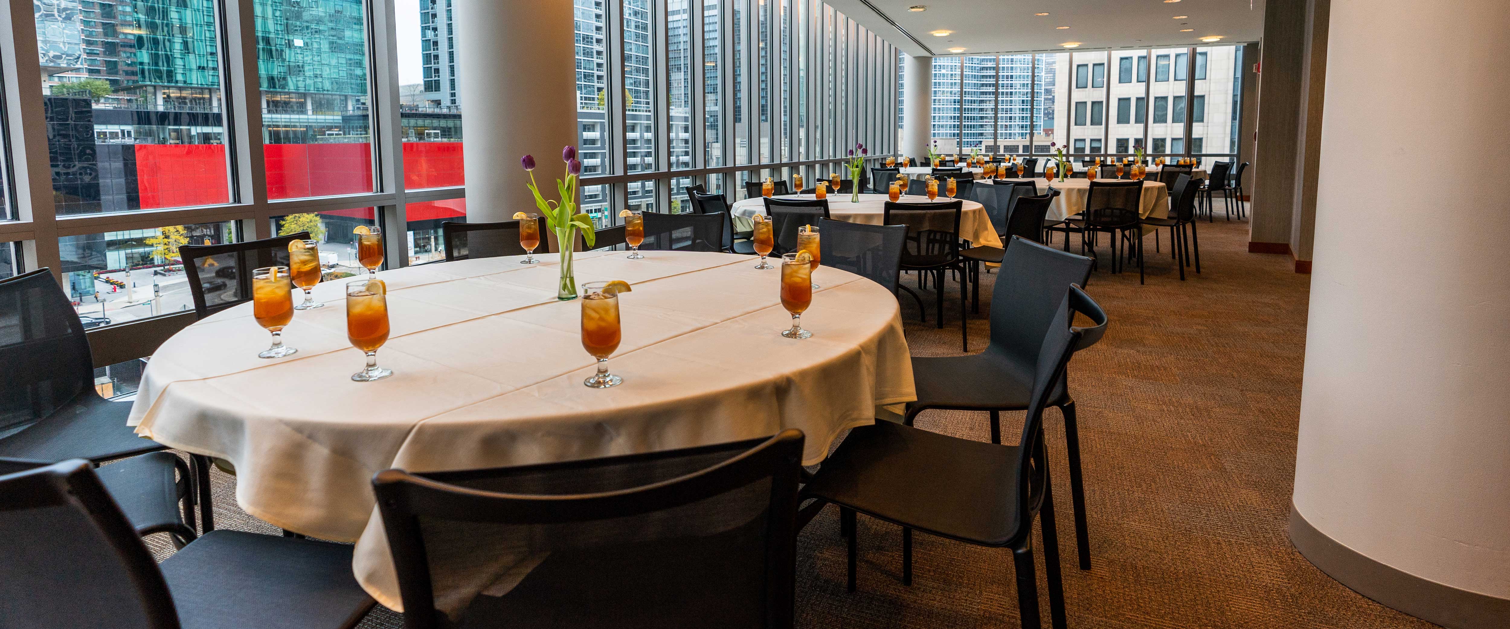 Chairs surround tables decorated with fresh cut flowers and iced tea
