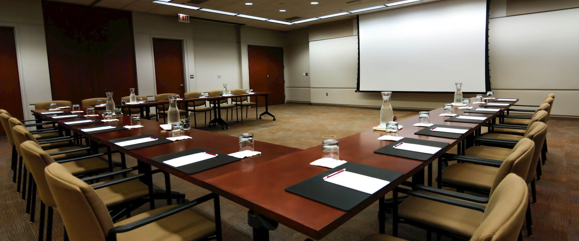 Angled view of warm wood tables in a U-shape facing a projector screen