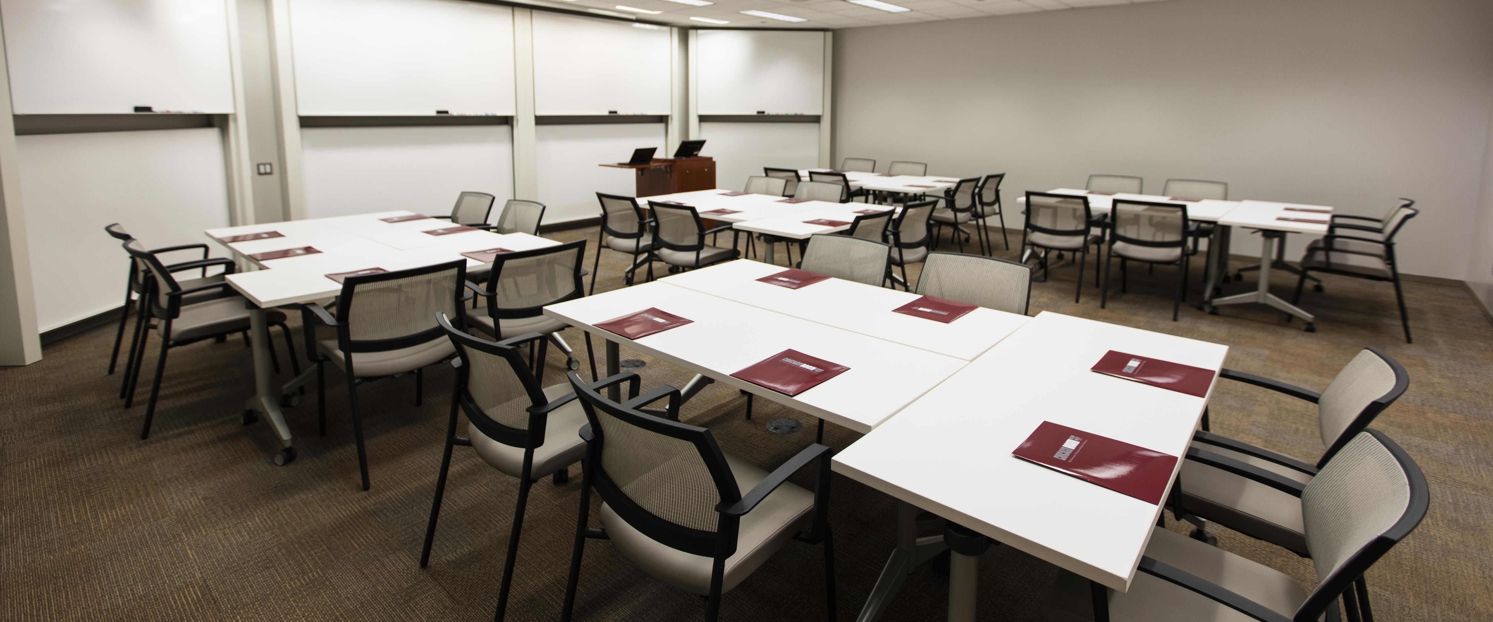 Classroom 303 in Gleacher Center looking toward the front with desks and chairs set up in pods of 6