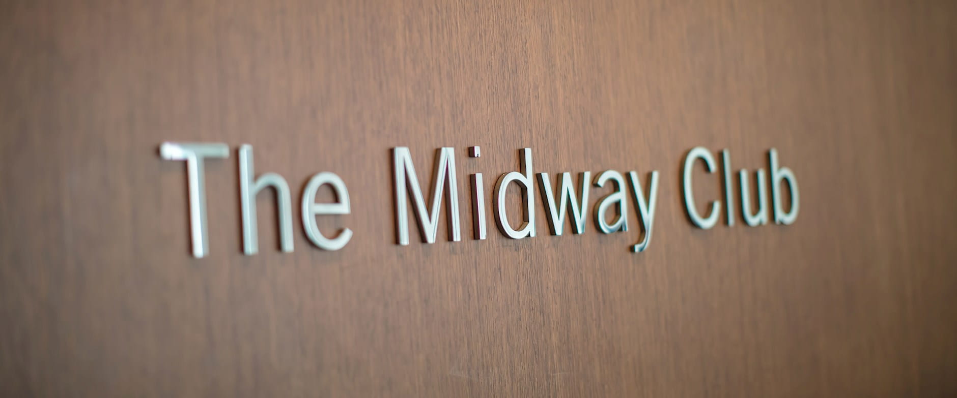 Metal signage which reads "The Midway Club" against dark panneled wood