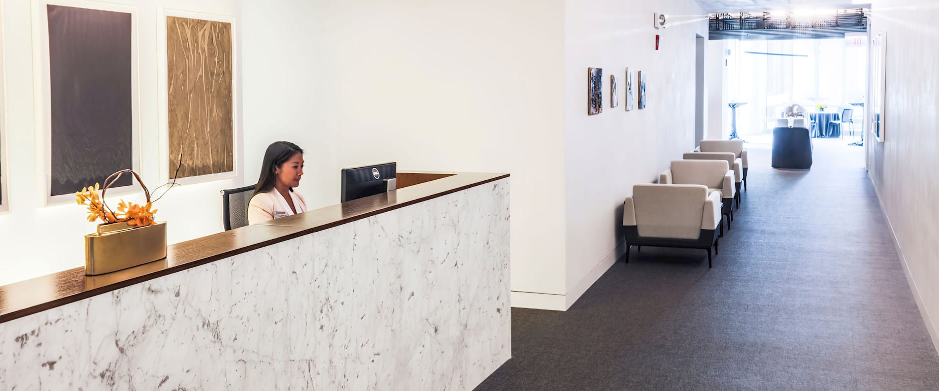 The PIMCO Midway Club at the Gleacher Center reception desk looking from the hallway into the room with a woman sitting behind a computer at the desk