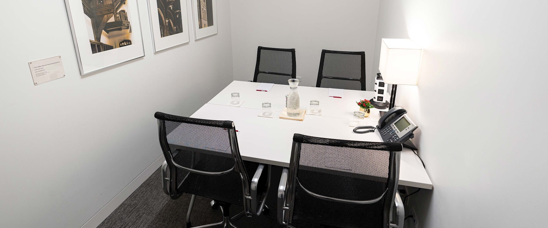Small executive board room with 4-person table set with water, notepads, and outlets